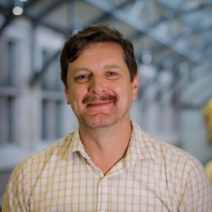 Photo of Alex Stonehill smiling and wearing a checkered shirt