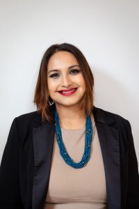 Head and shoulders image of a smiling woman with chin length hair and beaded necklace.