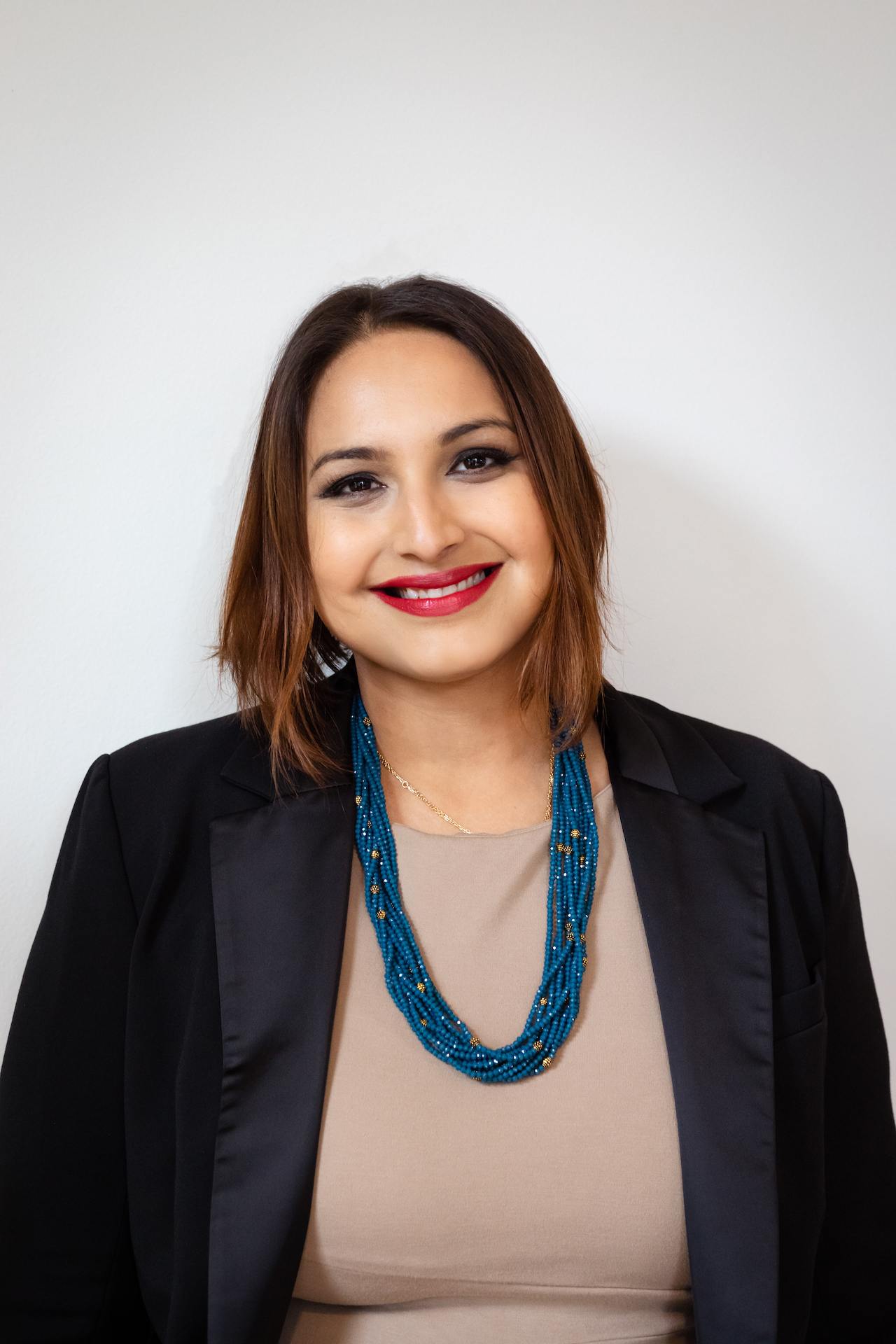 Head and shoulders image of a smiling woman with chin length hair and beaded necklace.